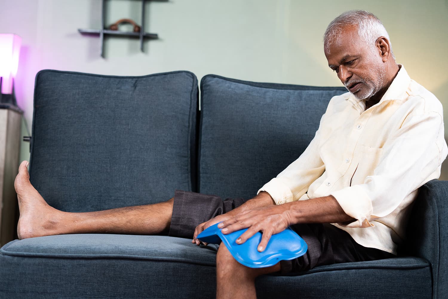 Man with pain sitting on couch with ice pack
